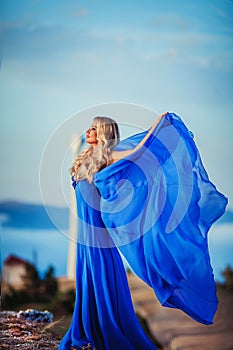 Sensual woman stand on the stone of peak mountain. blond woman with long hair walk on cliff`s edge and looking down on