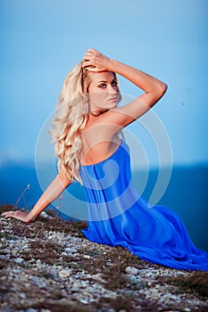 Sensual woman stand on the stone of peak mountain. blond woman with long hair walk on cliff`s edge and looking down on