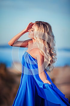 Sensual woman stand on the stone of peak mountain. blond woman with long hair walk on cliff`s edge and looking down on