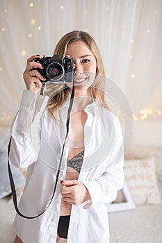 Sensual woman takes a photo of an old camera in bed