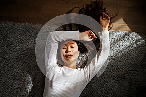 Sensual young asian woman with closed eyes lying on bed in sun light