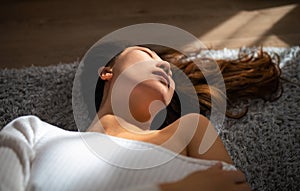 Sensual young asian woman with closed eyes lying on bed in sun light