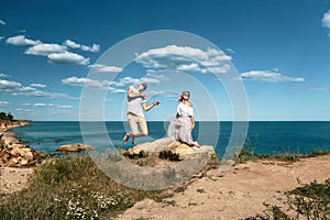 Sensual young couple in glasses in love jump on the rock in the sea near the beach with big cliffs. Man and woman looking on each