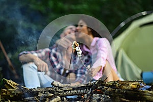 Sensual young couple in love roasting sweet marshmallow in fire and have fun together. Man and woman relaxing near