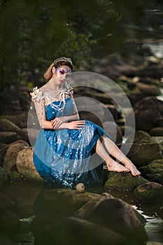 Sensual Young Mermaid of Sea in Artistic Caucasian Blond Woman With Strasses on Face Sitting in Blue Wet Dress on Rocky Shore