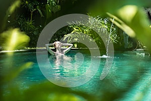 Sensual young woman relaxing in outdoor spa infinity swimming pool surrounded with lush tropical greenery of Ubud, Bali.