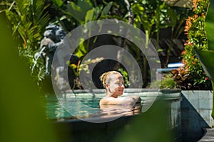 Sensual young woman relaxing in outdoor spa infinity swimming pool surrounded with lush tropical greenery of Ubud, Bali.