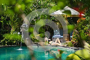 Sensual young woman relaxing in outdoor spa infinity swimming pool surrounded with lush tropical greenery of Ubud, Bali.