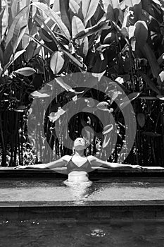 Sensual young woman relaxing in outdoor spa infinity swimming pool surrounded with lush tropical greenery of Ubud, Bali