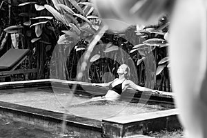 Sensual young woman relaxing in outdoor spa infinity swimming pool surrounded with lush tropical greenery of Ubud, Bali