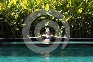 Sensual young woman relaxing in outdoor spa infinity swimming pool surrounded with lush tropical greenery of Ubud, Bali.