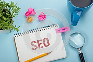 SEO, online concept. Notepad with message, pen, coffee cup and flower. Office supplies on desk table top view