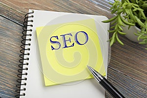 SEO, online concept. Notepad with message, pen and flower. Office supplies on desk table top view