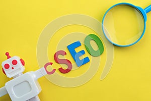 SEO Search engine optimization concept with vintage robot with magnifying glass, alphabet abbreviation SEO and robot on yellow