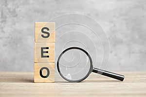 SEO Search Engine Optimization text wooden cube blocks and hand holding magnifying glass on table. Idea, Strategy, advertising,