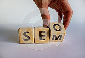 SEO versus SEM. Male hand turns a cube and changes the expression `SEO` to `SEM` or vice versa. Concept for SEO and SEM or Sea