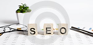 SEO word concept written on wooden blocks, cubes on a light table with flower ,pen and glasses on chart background