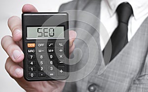 SEO word text inscription on calculator in a male hand of a businessman in white shirt and blue tie, Concept of finance and