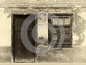 Sepia image of the facade of an old spanish house with shuttered window and old wooden door with faded plaster walls in strong s