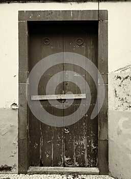 Sepia monochrome image of an old weathered wooden door nailed shut with a wooden bar and flaking paint on an outside wall