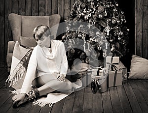 Sepia photo of a beautiful woman sitting in a room near Christmas tree