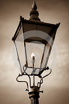 Sepia photo of retro street lamp shining against cloudy sky background