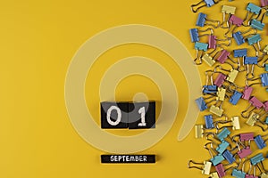 September 1 on a wooden calendar among colored clip for paper on a yellow background