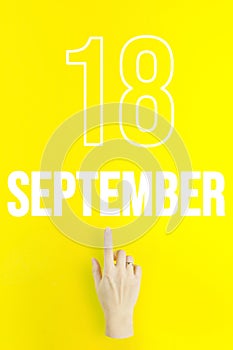 September 18th. Day 18 of month, Calendar date.Hand finger pointing at a calendar date on yellow background.Autumn month, day of