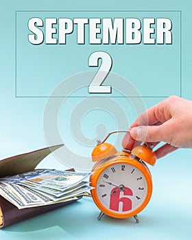 September 2nd. Hand holding an orange alarm clock, a wallet with cash and a calendar date. Day 2 of month.