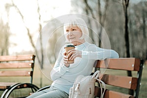 Septuagenarian granny taking pleasure of coffee on the park seat.