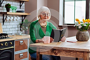 Septuagenarian silver-haired looking through Bible book sitting at kitchen table