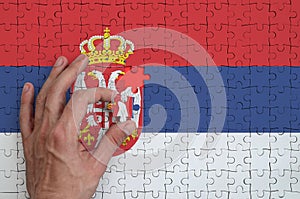 Serbia flag is depicted on a puzzle, which the man`s hand completes to fold