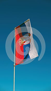 Serbian flag flapping on a pole with blue sky as background