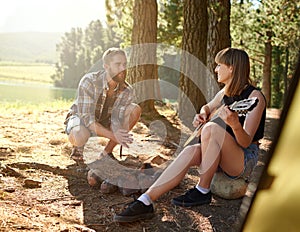 Serenading in the outdoors. a young woman playing guitar for her boyfriend at their campsite.
