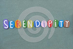 Serendipity, creative word composed with multi colored stone letters over green sand photo