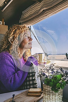 Serene adult woman admiring nature beach sitting inside a modern camper van in travel holiday vacation. Pretty young female people