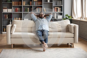 Serene barefoot african man resting on sofa hands behind head