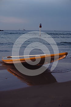 Serene beachscape with a flipped yellow kayak on sand, tranquil sea, twilight sky, and distant sailboats