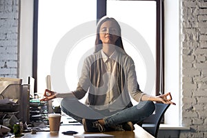 Serene calm business woman sit on office desk meditating