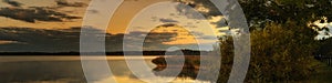 a serene calm morning on a lake with coastal reeds and trees in the warm light of dawn. widescreen panoramic view landscape