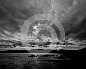 Serene coastal scene featuring a pier stretching out into a cloudy sky above tranquil waters