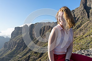 Serene Cute Tourist woman, laughing and admiring the freedom and the landscape in the mountain, sitting in a rock. Model sit and