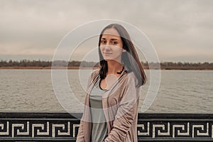 Serene girl standing alone on waterfront in front of fence