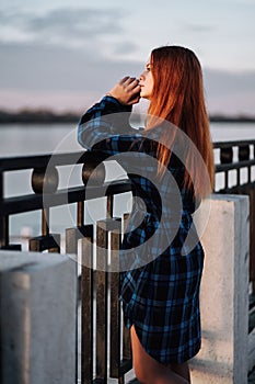 Serene girl standing alone on waterfront in front of fence of embankment.