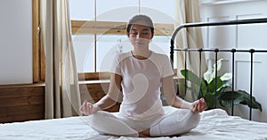 Serene healthy asian girl meditating with eyes closed in bed