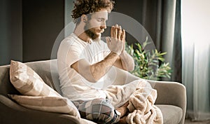 Serene Man Meditates in lotus Position on His Couch At Home. A Man With Folded Hands Prays in the Morning. Close-up
