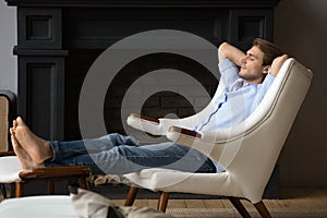 Serene man put feet on footstool relaxing in armchair