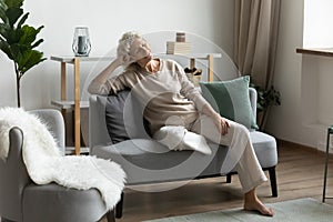 Serene mature 60s woman relaxing in modern comfortable living room