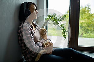 Serene Moment as Woman in Headphones Embraces Cat by Window in Daylight