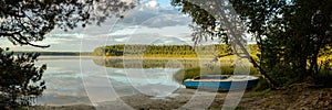 Serene morning landscape. panoramic view from the shore of a large lake with a fishing boat, sky reflection on the water, a forest